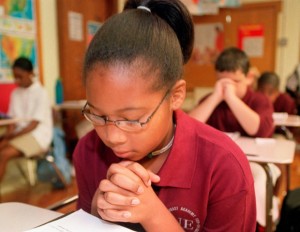 Young black girl praying at her desk in school