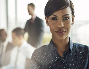 Close up on smiling beautiful business woman with light flare over shoulder from large window in office with group