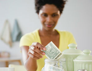 a black woman in a yellow t-shirt putting money away in a glass jar