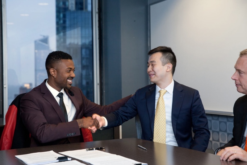 Ray J and Ray Lee of Cowboy Wholesale shake hands after signing the paperwork cementing their $31 million Raycon distribution deal. (Image: Raycon)