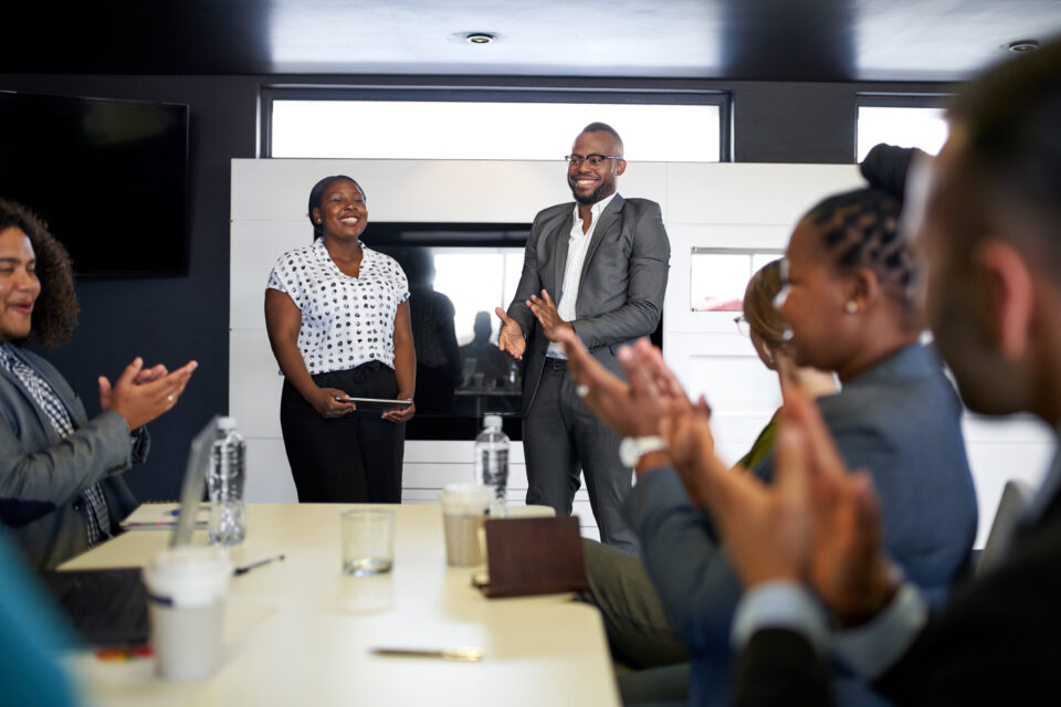 Black businessman being encouraged by diverse multi-ethnic group of coworkers during presentation in office