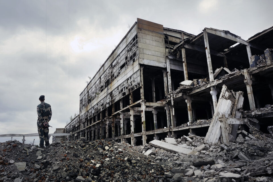 Soldier in military uniform stands on the ruins of destroyed property